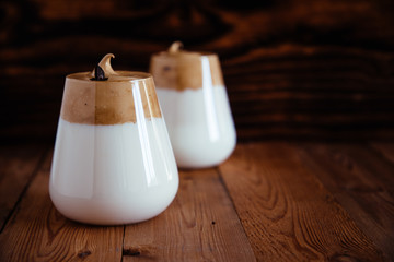 Whipped Dalgona coffee in a clear coffee mug on a wooden table.