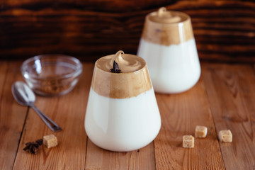Whipped Dalgona coffee in a clear coffee mug on a wooden table.