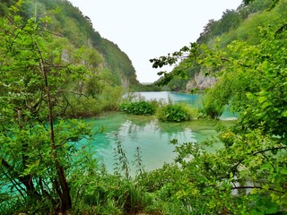 Imagen primaveral de pasarelas flotantes de madera junto a cascadas y lagos azules con antiguos...