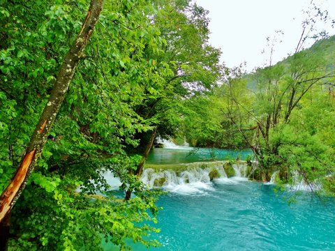 Imagen primaveral de pasarelas flotantes de madera junto a cascadas y lagos azules con antiguos embarcaderos y barcas de remos en plena naturaleza en el Parque Nacional de los Lagos de Plitvice