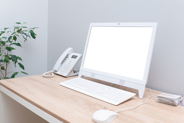 Isolated white computer display for mockup on desk in bright cozy office with white computer mouse and telephone