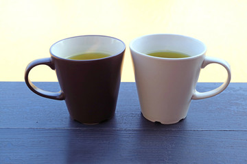 Two cups of green tea on a waterfront wooden table with selective focus