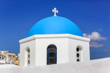 Fototapeta na wymiar Close-up of the round dome of the Church with a blue cross, white stone walls against the blue sky in Greece on Santorini