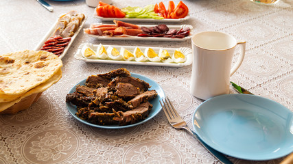breakfast table: chopped vegetables, sliced meat, boiled eggs on long white porcelain plates on a white tablecloth