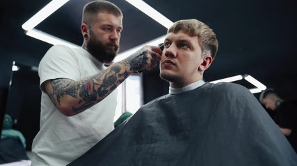 Male haircut with electric razor. Close up of hair trimmer hairstyle. Barber makes haircut for client at the barber shop by using hairclipper. Man hairdressing with electric shaver. Handheld shot. 4K.