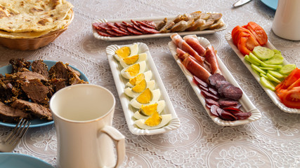 breakfast table: chopped vegetables, sliced meat, boiled eggs on long white porcelain plates on a white tablecloth