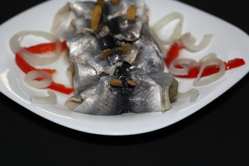 Pickled herrings called rollmops with pieces of onion and red pepper on white plate macro close up, black background