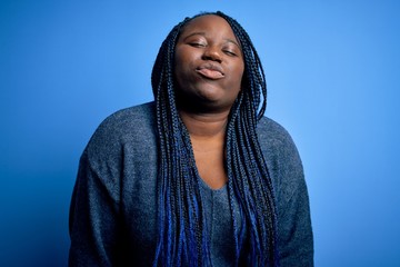 African american plus size woman with braids wearing casual sweater over blue background looking at the camera blowing a kiss on air being lovely and sexy. Love expression.