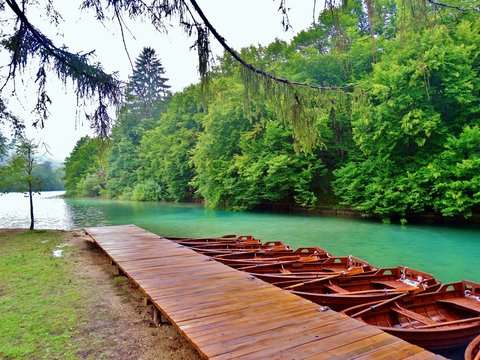 Imagen primaveral de pasarelas flotantes de madera junto a cascadas y lagos azules con antiguos embarcaderos y barcas de remos en plena naturaleza en el Parque Nacional de los Lagos de Plitvice