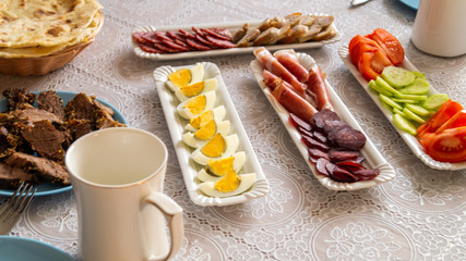 breakfast table: chopped vegetables, sliced meat, boiled eggs on long white porcelain plates on a white tablecloth