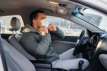 A young man sits behind the wheel wearing a mask for personal safety while driving during a pandemic and coronavirus. Epidemic