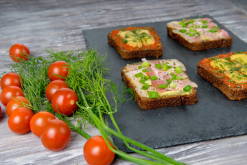 Sandwiches made from slices of bread with bacon, cheese and herbs are served with fresh green dill and red cherry tomatoes. Fast, nutritious and highcalorie breakfast food. side view