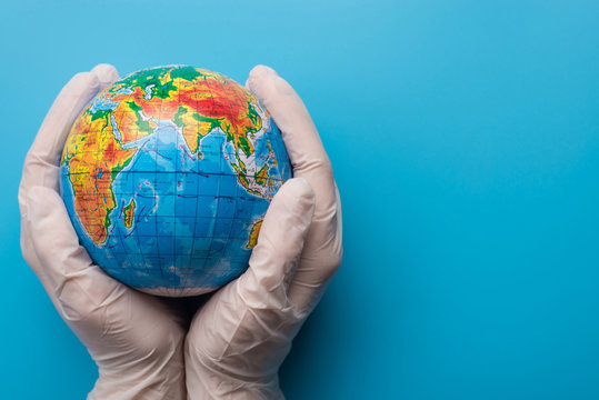 Save the planet concept. A person wearing gloves holds small planet earth isolated on blue background