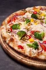 Vegetable pizza on a wooden board. Dark background.