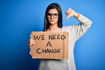 Young beautiful brunette activist woman holding banner protesting to change with angry face,...