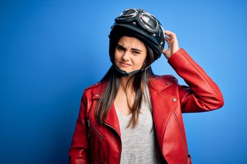 Young beautiful brunette motorcycliste woman wearing motorcycle helmet and jacket confuse and wonder about question. Uncertain with doubt, thinking with hand on head. Pensive concept.