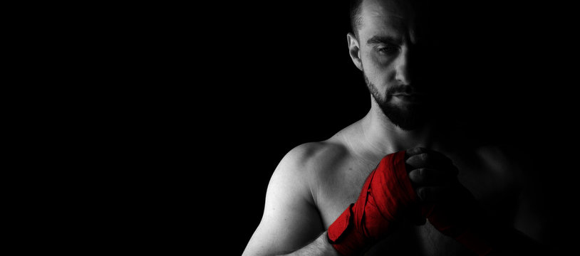 Banner image of a man’s fighter with a beard and red bandages on his hands. Black white image with red. Place for text. Black background.