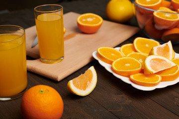 Fresh orange fruit whole and sliced on a wooden table, cutting board and kitchen knife. A plate full of citrus slices - natural and healthy food. Glass of fruit cocktail.