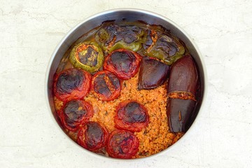 Gemista, stuffed tomatoes and peppers freshly cooked Greek traditional food in a roasting pan isolated on a white marble table. Top view