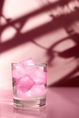 Glass with colored ice on a pink background with beautiful shadows.