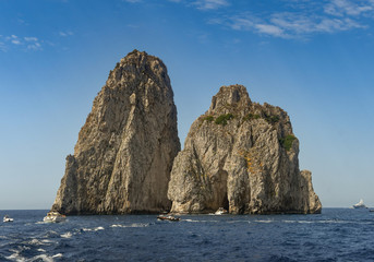 Wide angle view of the Faraglioni rock formation off the coast of Capri. Small boats are approaching the arch.