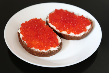Sandwiches with red caviar, butter and rye bread on white plate, selective focus. Traditional russian dish