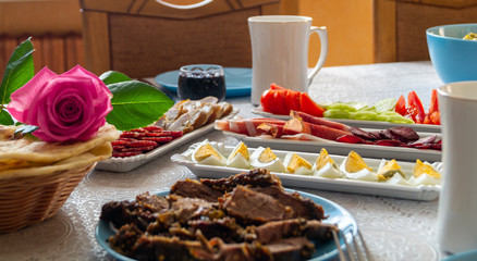 breakfast table: chopped vegetables, sliced meat, boiled eggs on long white porcelain plates on a white tablecloth