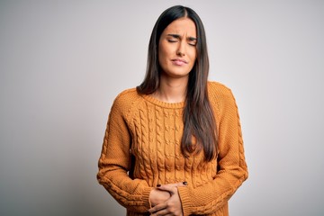 Young beautiful brunette woman wearing casual sweater over isolated white background with hand on...