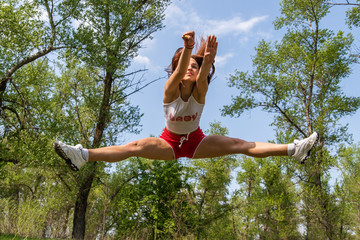 Young athletic girl doing an acrobatic stunt in the air. Jump Twine. Doing sport outside