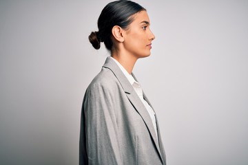 Young beautiful brunette businesswoman wearing jacket standing over white background looking to...