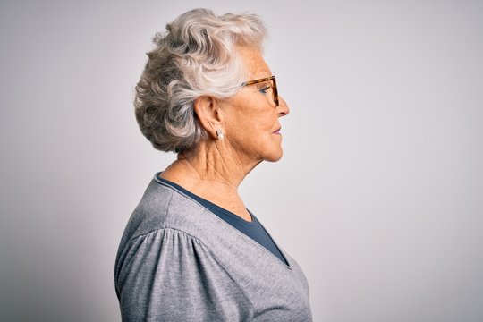Senior beautiful grey-haired woman wearing casual sweater and glasses over white background looking to side, relax profile pose with natural face with confident smile.
