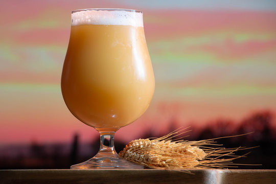 Poured glass of a creamy, hazy India pale ale craft beer from a small micro brewer, with a sunset farm background.