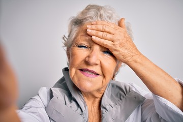 Senior beautiful grey-haired woman making selfie by camera over isolated white background stressed with hand on head, shocked with shame and surprise face, angry and frustrated. Fear and upset