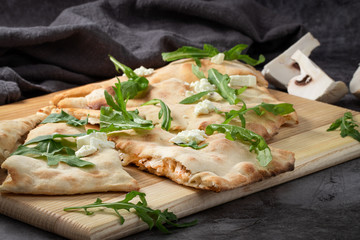 calzone with fresh arugula and mushrooms on a dark background