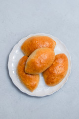 Russian bakery pirozhki (stuffed buns) on white plate on neutral concrete background. Top view, space for text