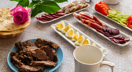 breakfast table: chopped vegetables, sliced meat, boiled eggs on long white porcelain plates on a white tablecloth