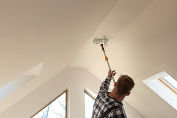 Home improvement concept, handyman painting a wall with a white paint near roof window in attic