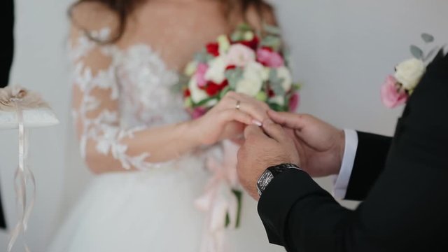 The groom puts a golden wedding ring on the brides finger. The bride and groom are engaged.