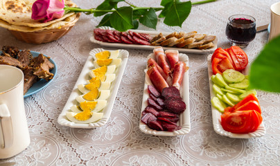 breakfast table: chopped vegetables, sliced meat, boiled eggs on long white porcelain plates on a white tablecloth