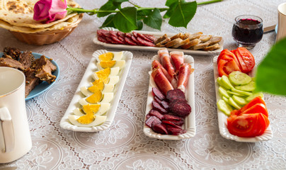 breakfast table: chopped vegetables, sliced meat, boiled eggs on long white porcelain plates on a white tablecloth