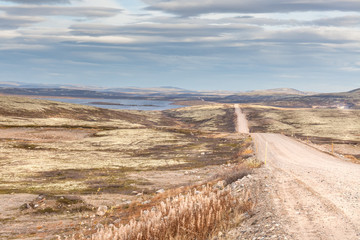 Gravel road to Teriberka in northern tundra landscape of Kola Peninsula. Natural scenery in autumn season. Murmansk Oblast, Russia