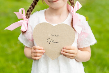 I love you mum written on a heart shaped card held by a girl on grass background