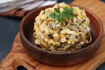Salad with beans, eggs and champignons in a brown plate on wooden board, Closeup