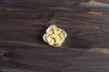 portion of cashews in a paper muffin cup on a dark wood background