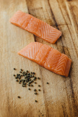 Two pieces of raw salmon on wooden table and a handful of black pepper top view. Ingredients for dinner or for sushi. Healthy fats, good fats concept. Vertical photo