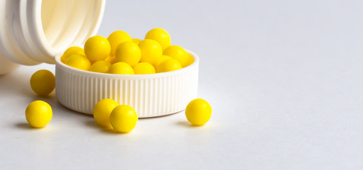 Round yellow vitamins are poured out on a white glossy table from a white plastic bottle. Concept. Place for the label. Diagnosis.