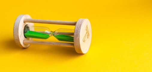 Hourglass with green sand inside on a yellow background
