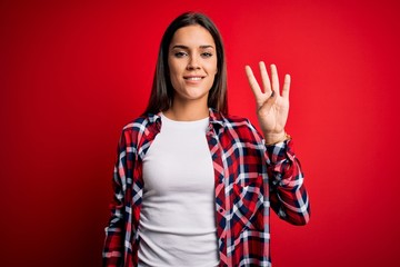 Young beautiful brunette woman wearing casual shirt standing over isolated red background showing and pointing up with fingers number four while smiling confident and happy.