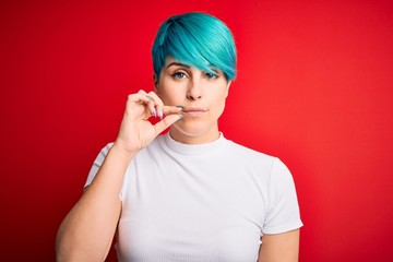 Young beautiful woman with blue fashion hair wearing casual t-shirt over red background mouth and lips shut as zip with fingers. Secret and silent, taboo talking