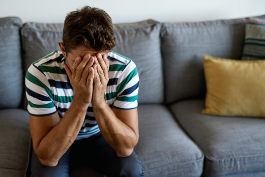 Young man sitting on his sofa looking distraught